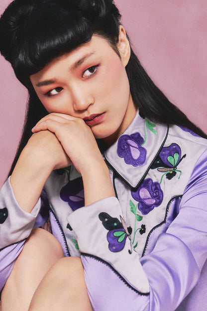 Person wearing a light lilac outfit with dark lilac and pink floral embroidery, collar and wrist