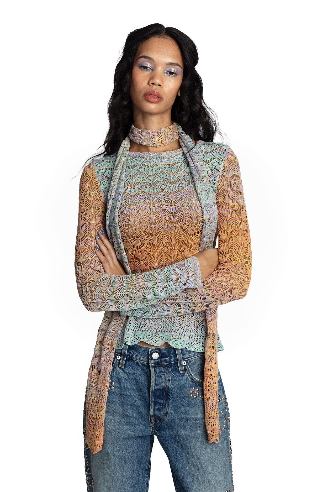 Women wearing a long sleeve gradient crochet top with matching long, thin scarf and jeans with her arms crossed on a white background.