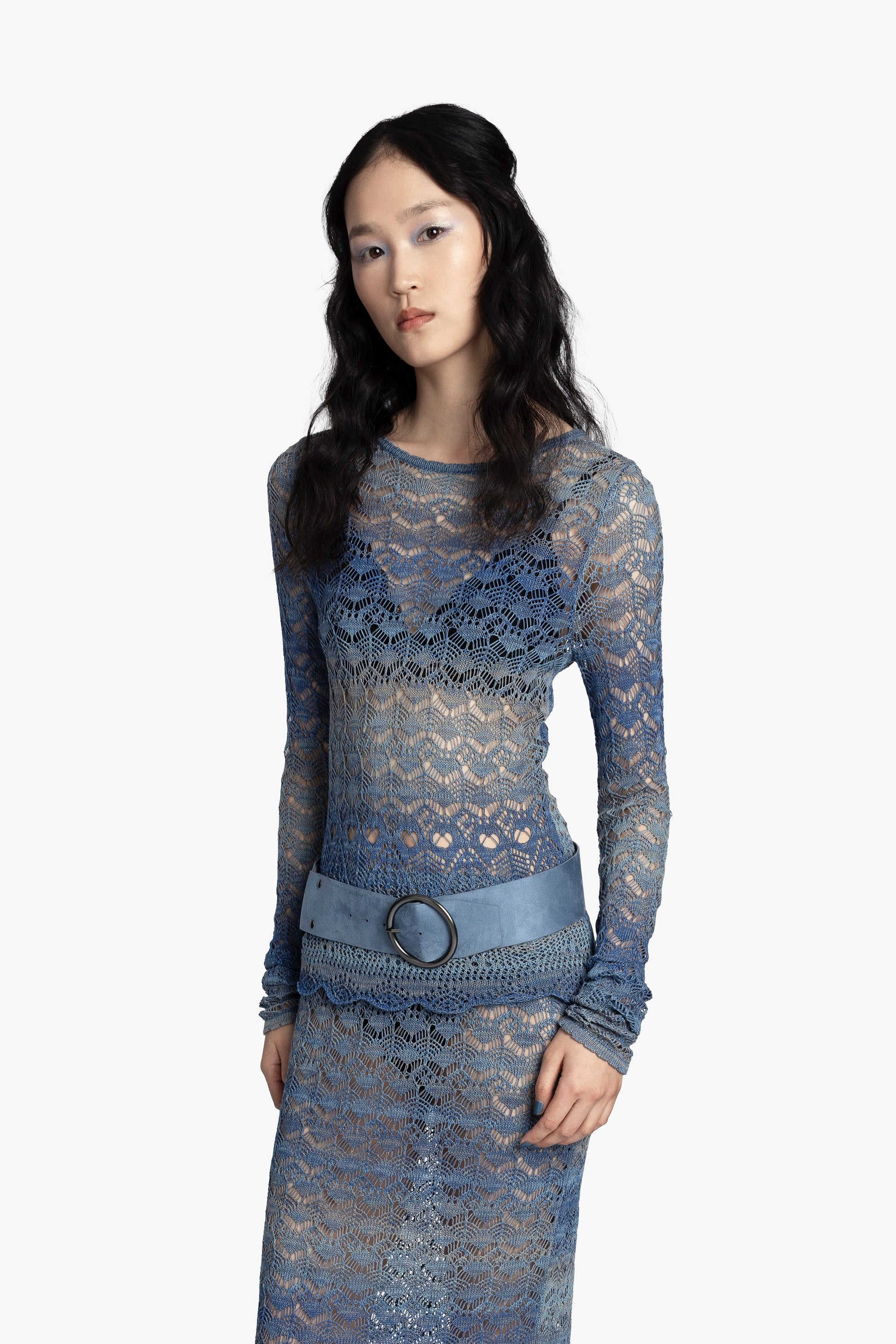 Woman wearing a blue crochet top and matching skirt with a blue belt on a white background.