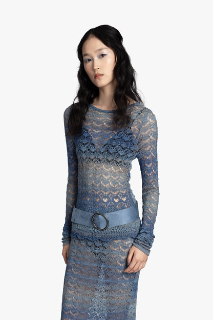 Woman wearing a blue crochet top and matching skirt with a blue belt on a white background.