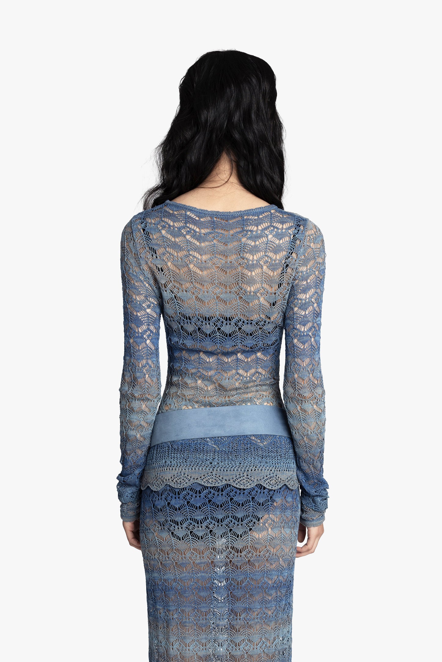 Back view of a woman wearing a blue crochet top and matching skirt with a blue belt on a white background.