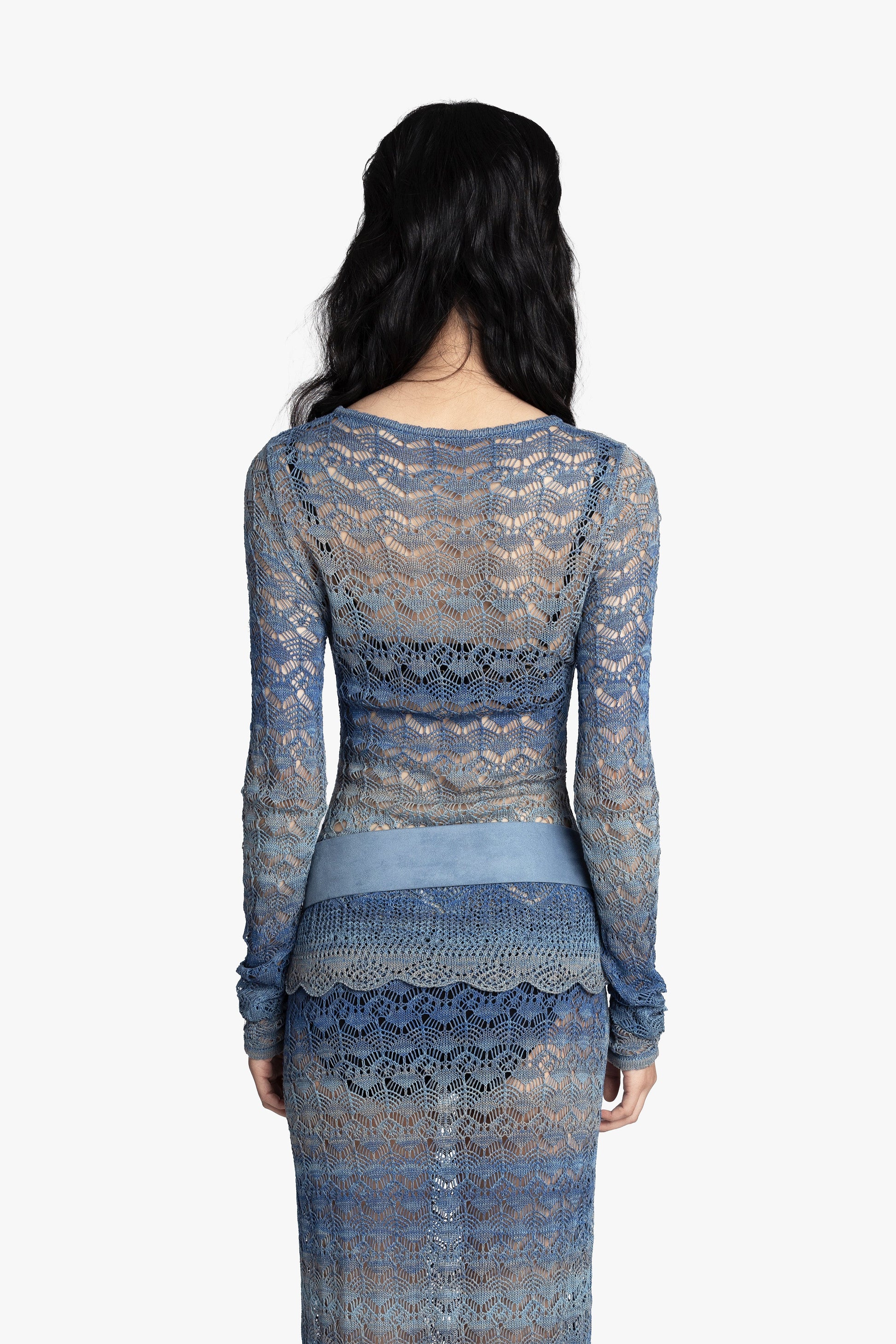 Back view of a woman wearing a blue crochet top and matching skirt with a blue belt on a white background.