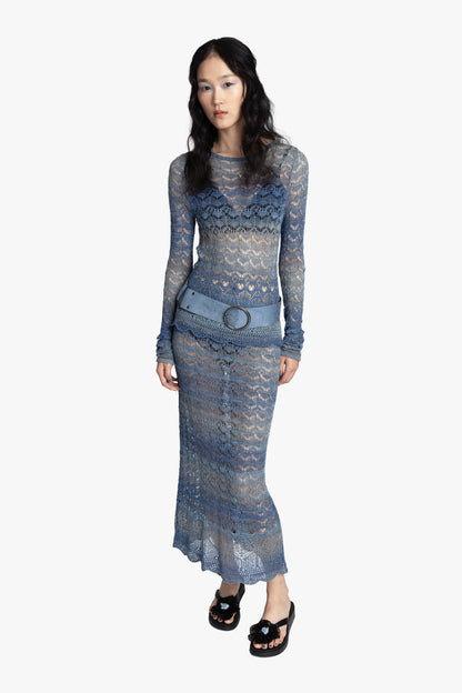 Woman wearing a blue crochet top and matching skirt with a blue belt on a white background.