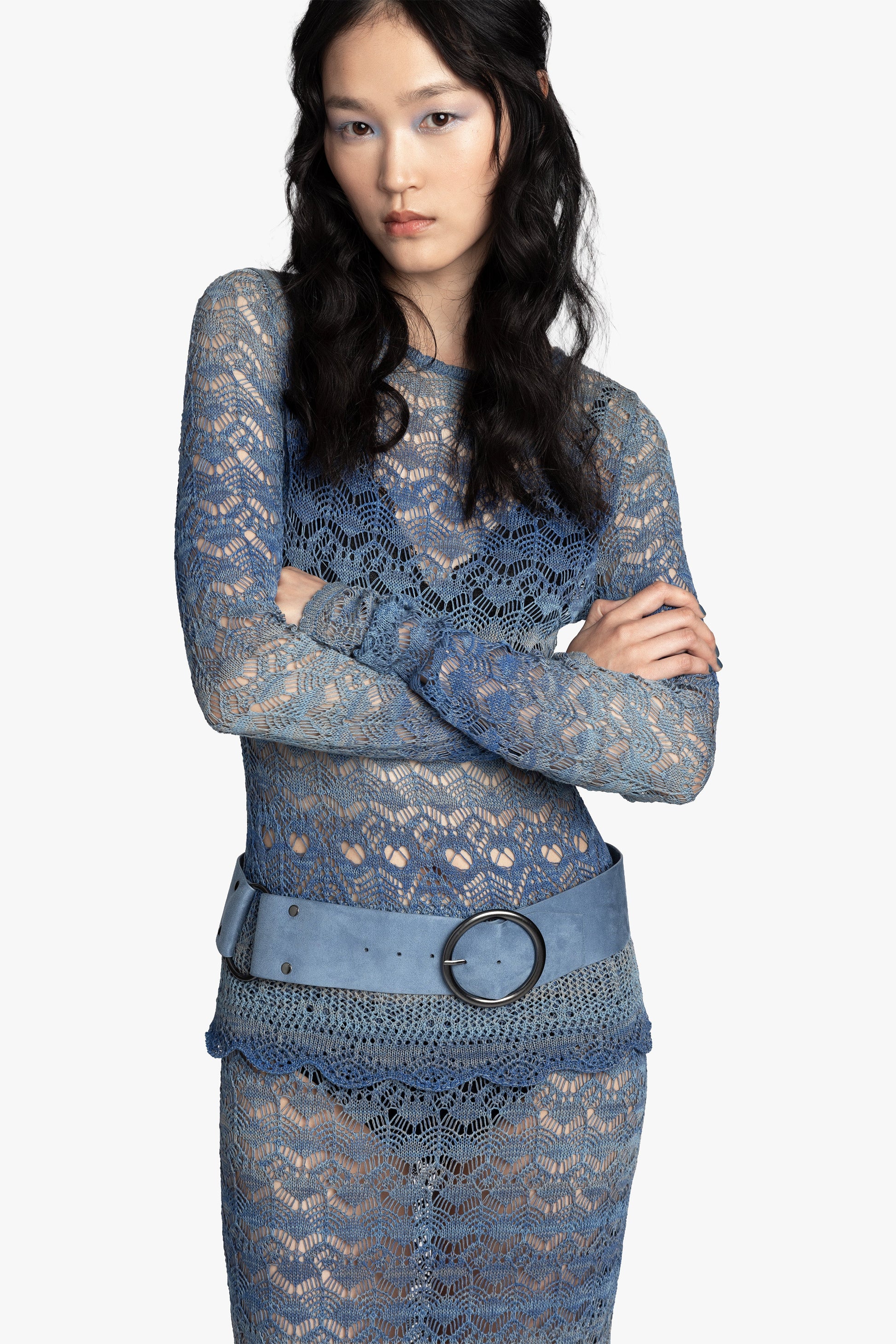 Woman wearing a blue gradient crochet outfit with a blue belt on a white background.