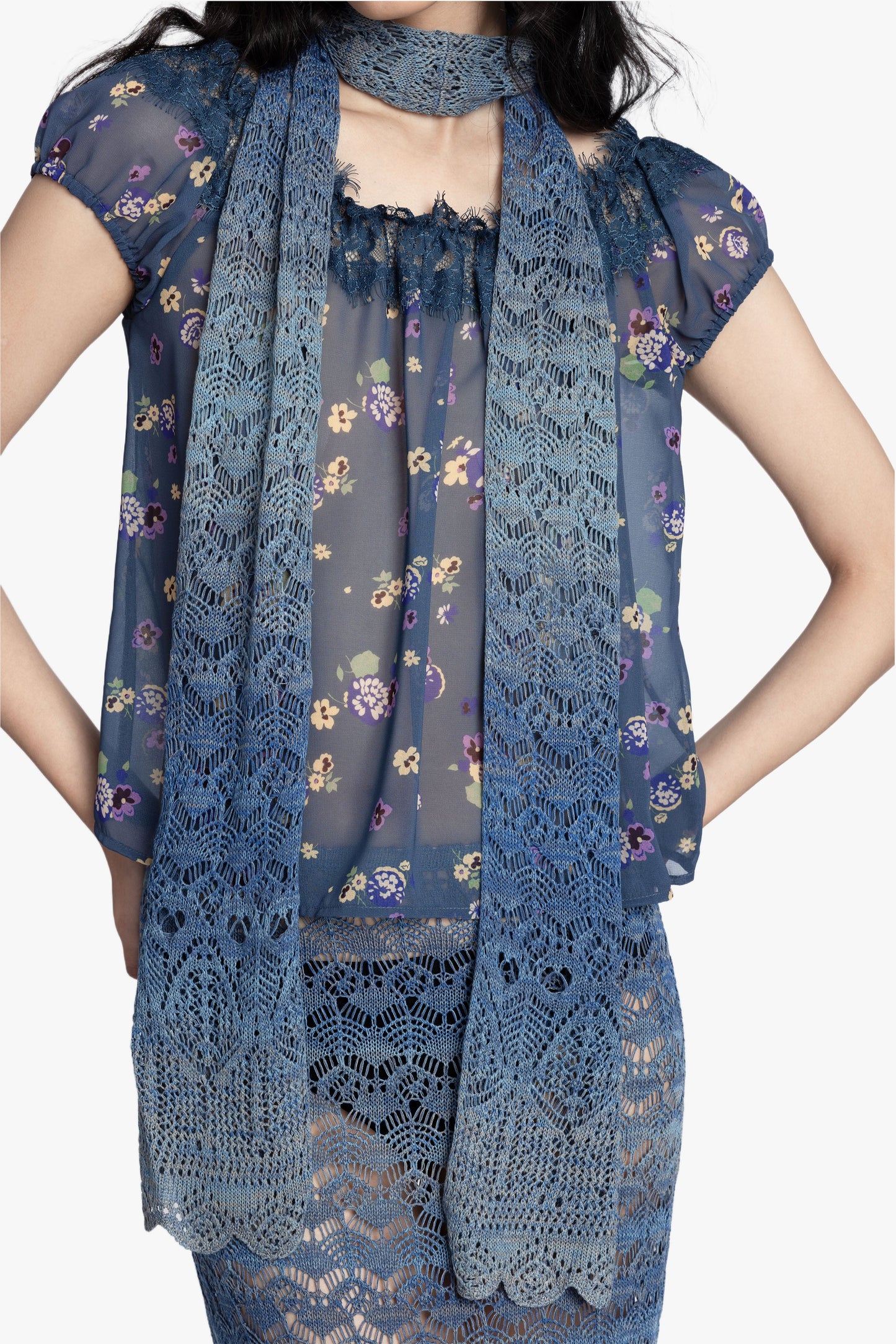 Woman wearing a blue floral short sleeve top, blue gradient crochet scarf and matching skirt on a white background.