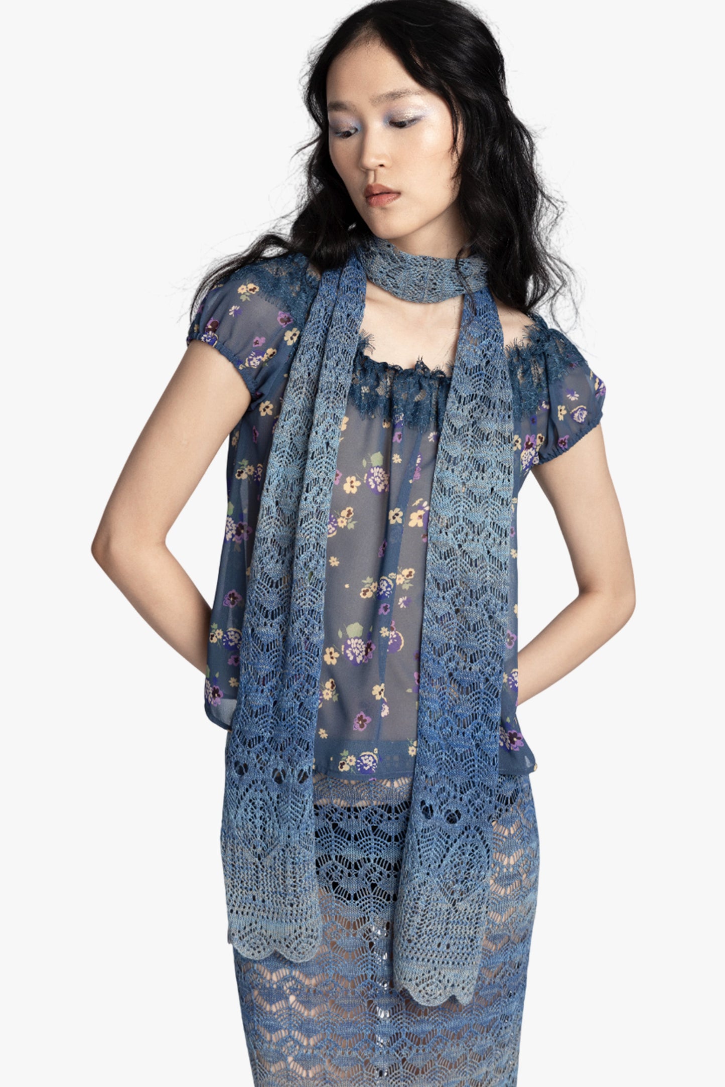 Woman wearing a blue floral short sleeve top, blue gradient crochet scarf and matching skirt on a white background.