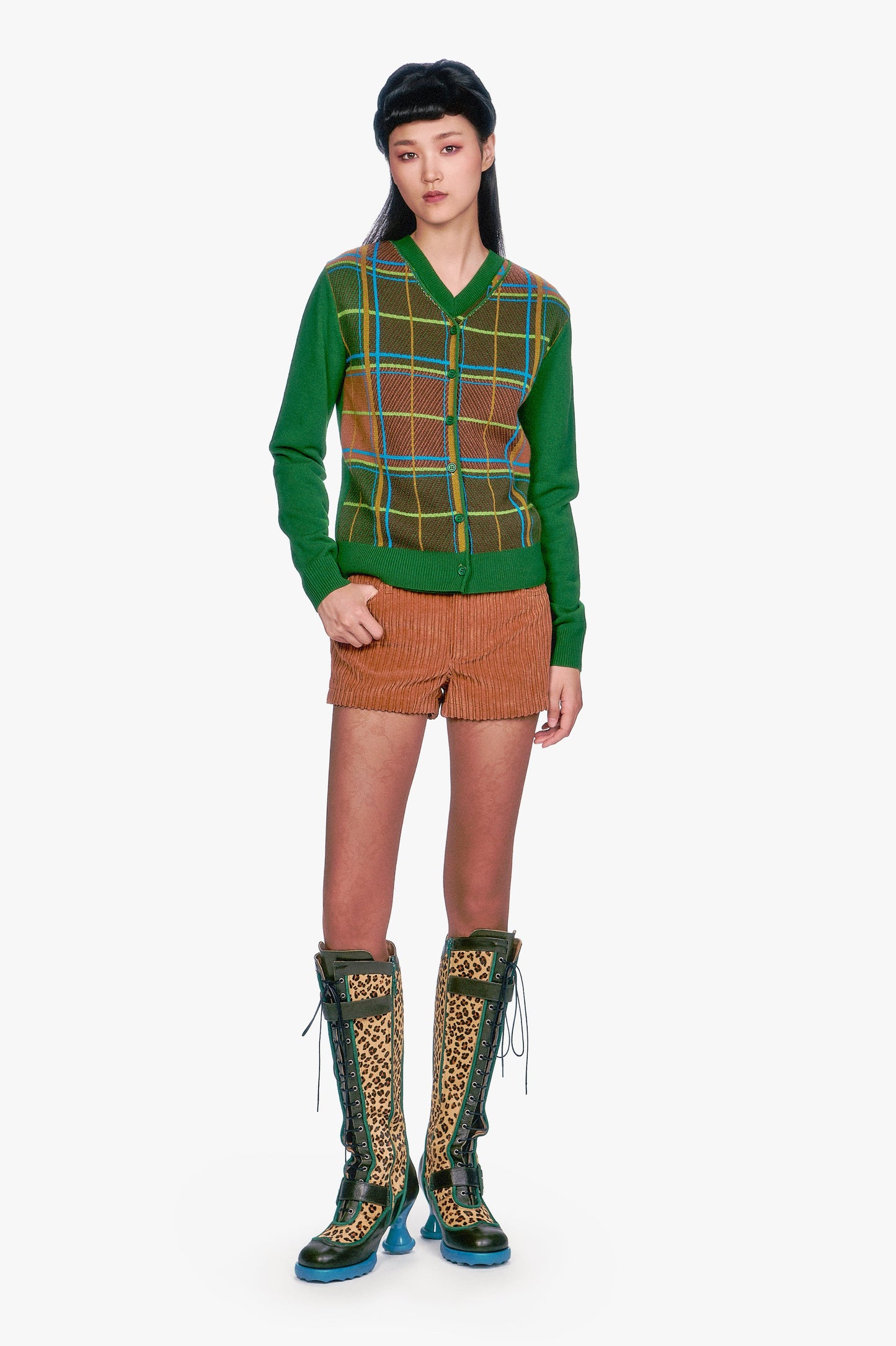 Person wearing a Plaid Cardigan, Leaf Green vest with brown shorts, and leopard print boots