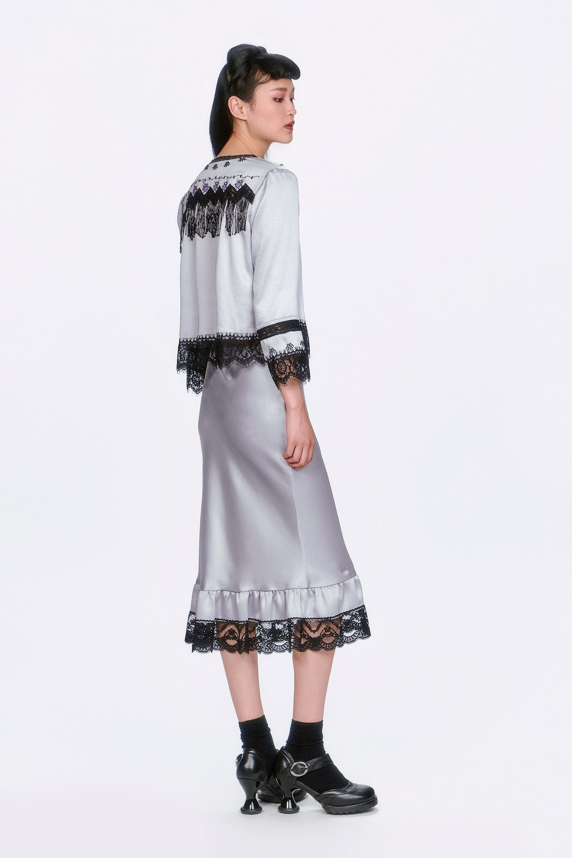Woman wearing Boudoir Satin Beaded Fringe Bed Silver Jacket and skirt with black lace details.