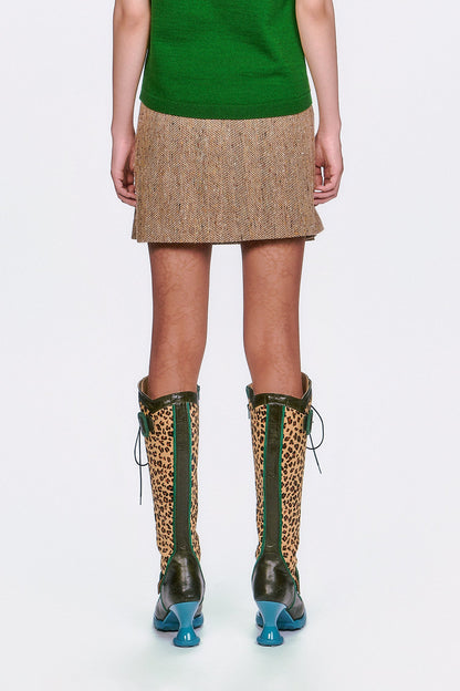 A woman wearing The Herringbone Pleated Skirt Caramel mid-tight high, green top & leopard print boots