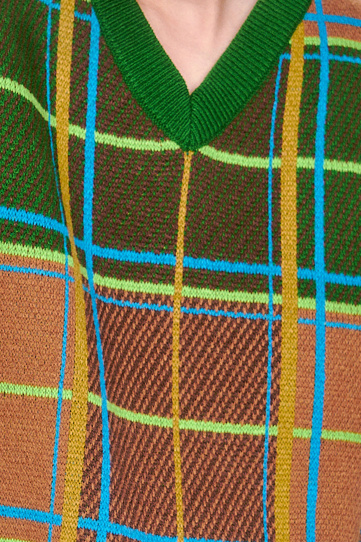 Close-up of a plaid fabric pattern, intersecting lines in green, brown, and blue, forming a grid of squares