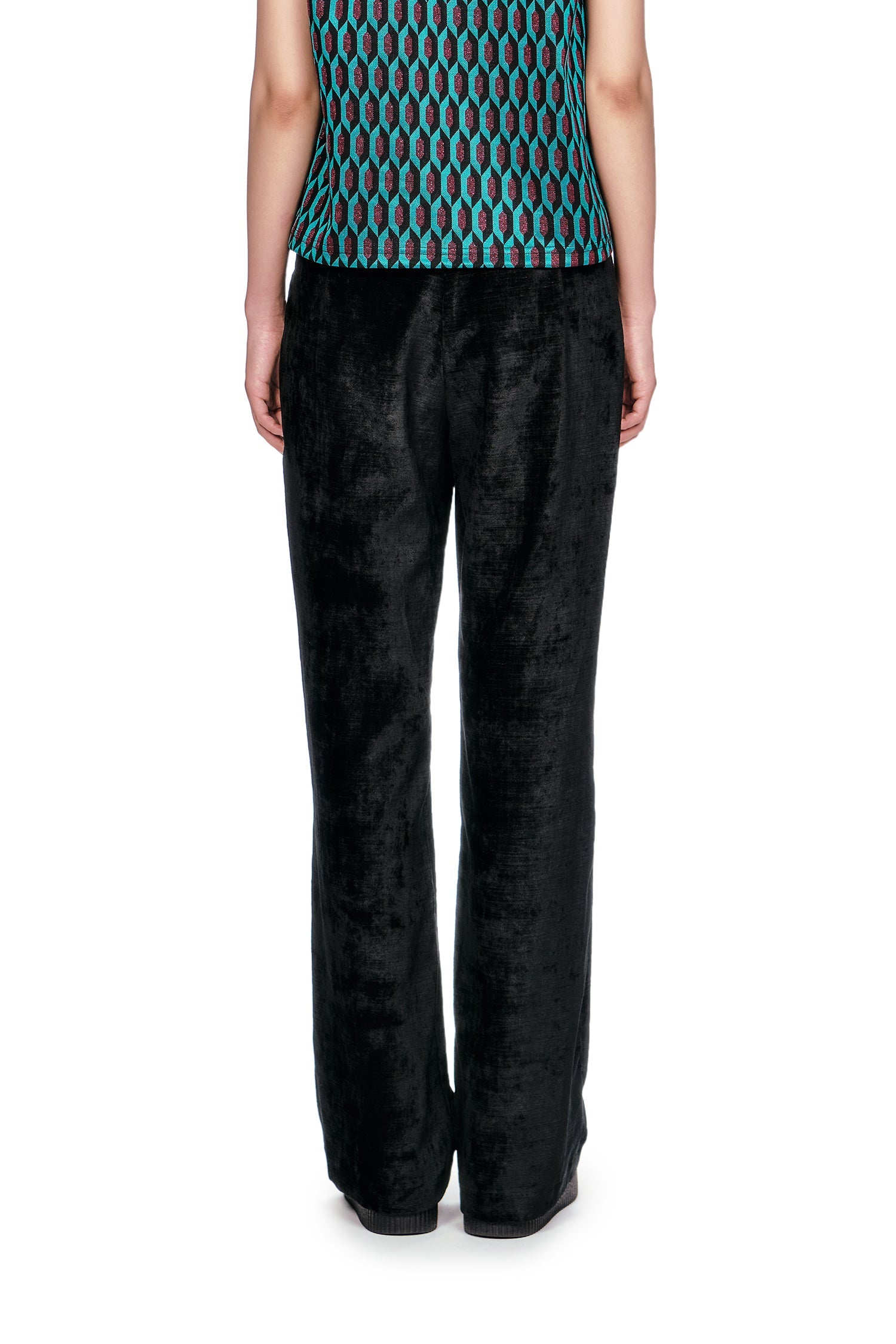 Person wearing a patterned sleeveless top and black Velour pants and black shoes.