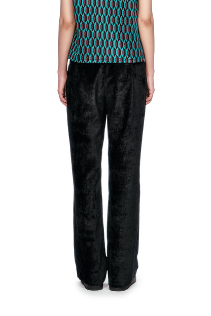 Person wearing a patterned sleeveless top and black Velour pants and black shoes.