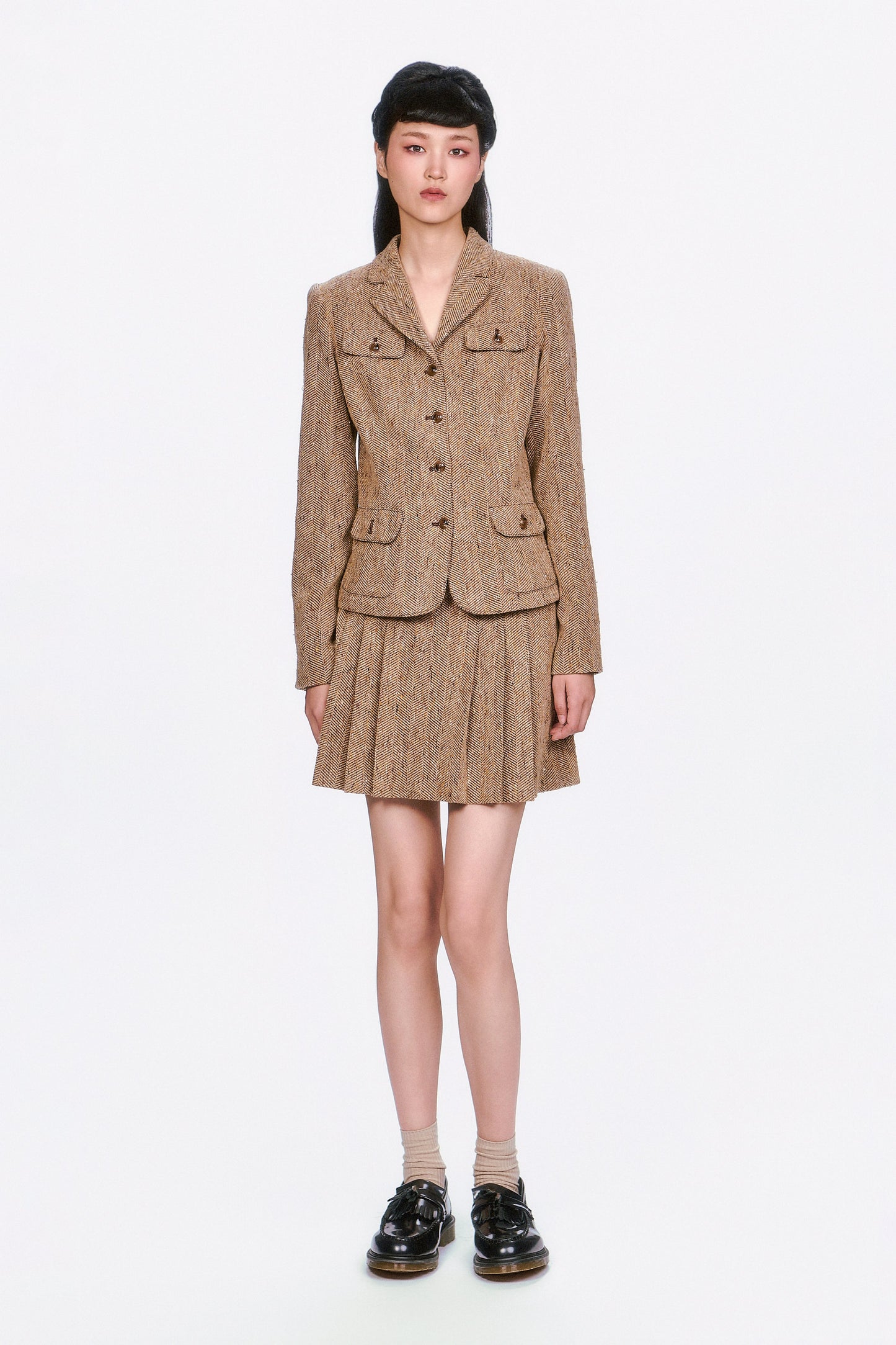 Woman wearing a Herringbone brown tweed jacket and Herringbone brown pleated skirt.