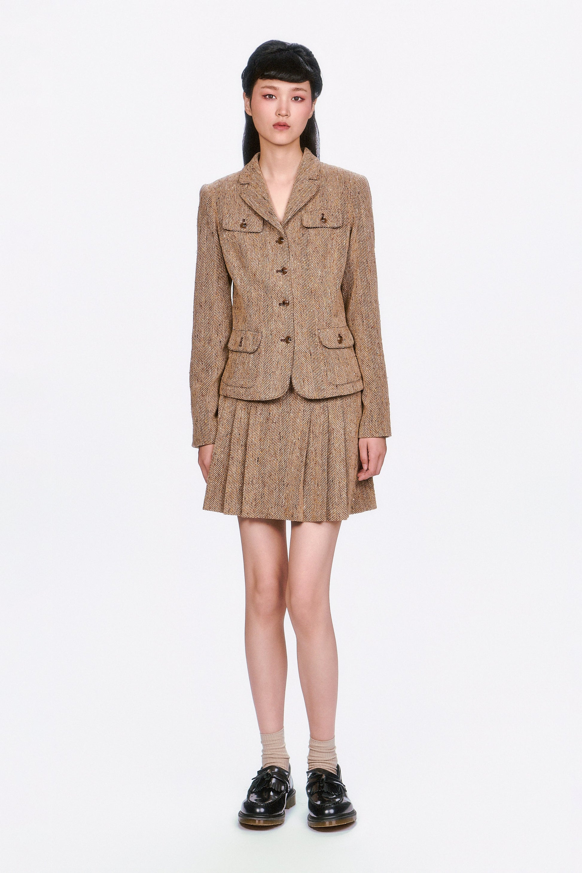 Woman wearing a Herringbone brown tweed jacket and Herringbone brown pleated skirt.