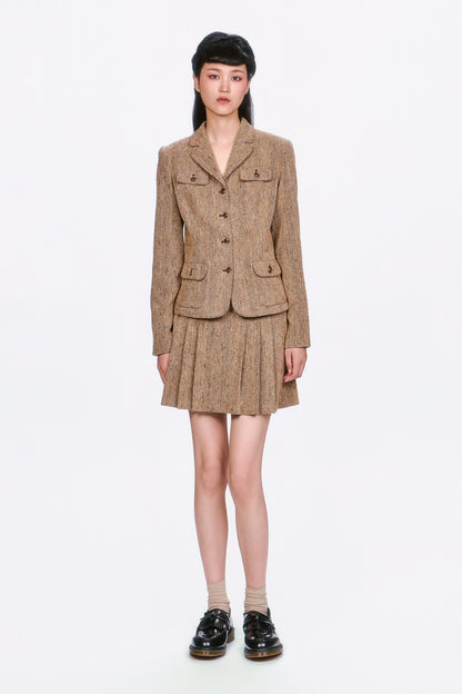 Woman wearing a Herringbone brown tweed jacket and Herringbone brown pleated skirt.