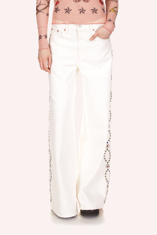 White jean, 2 front pockets, front zipper, wide legs over shoes, oval studded shapes, with silver/copper, top to bottom