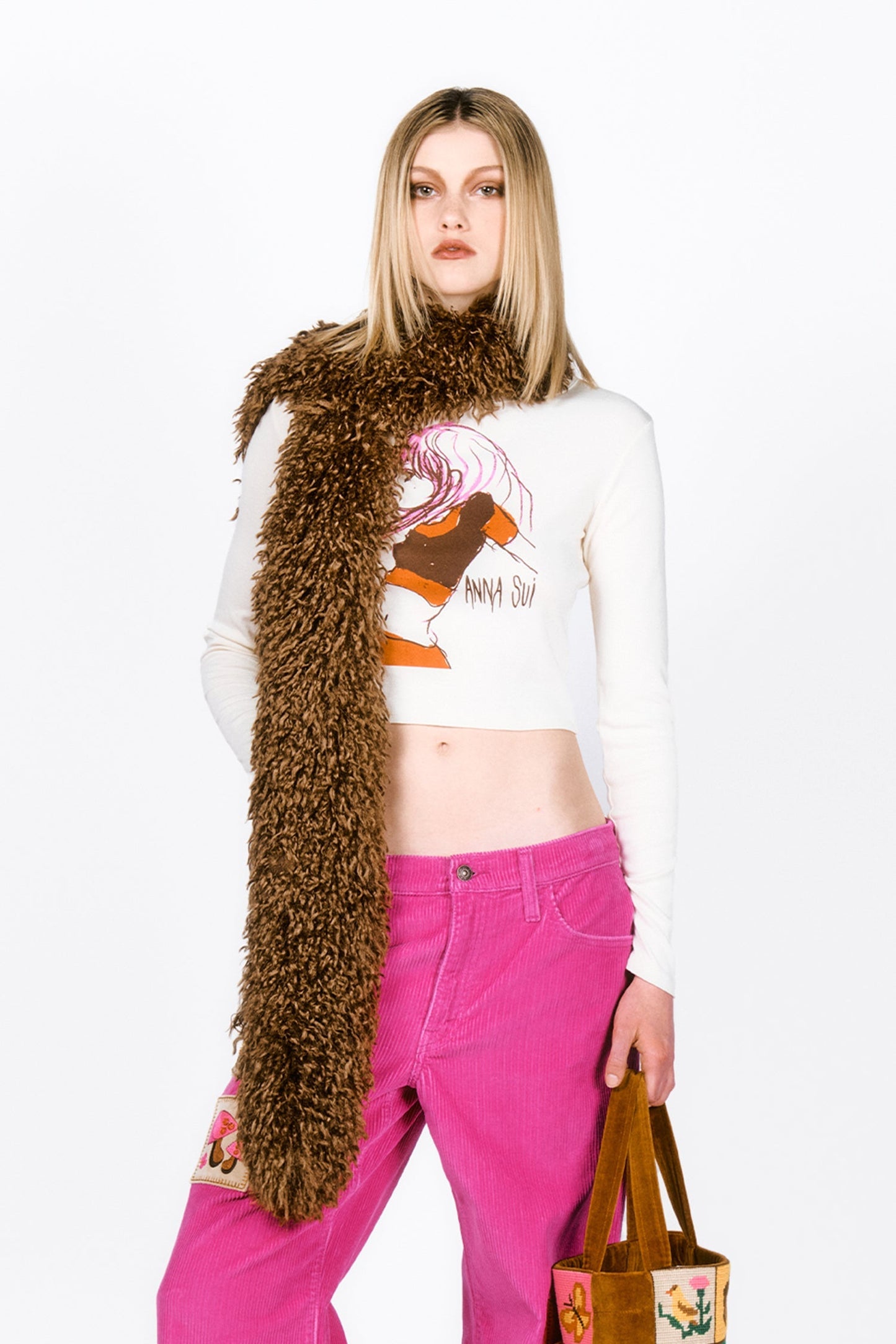 Woman wearing a Faux Fur Scarf - Caramel, white crop top with graphic design, and pink pants