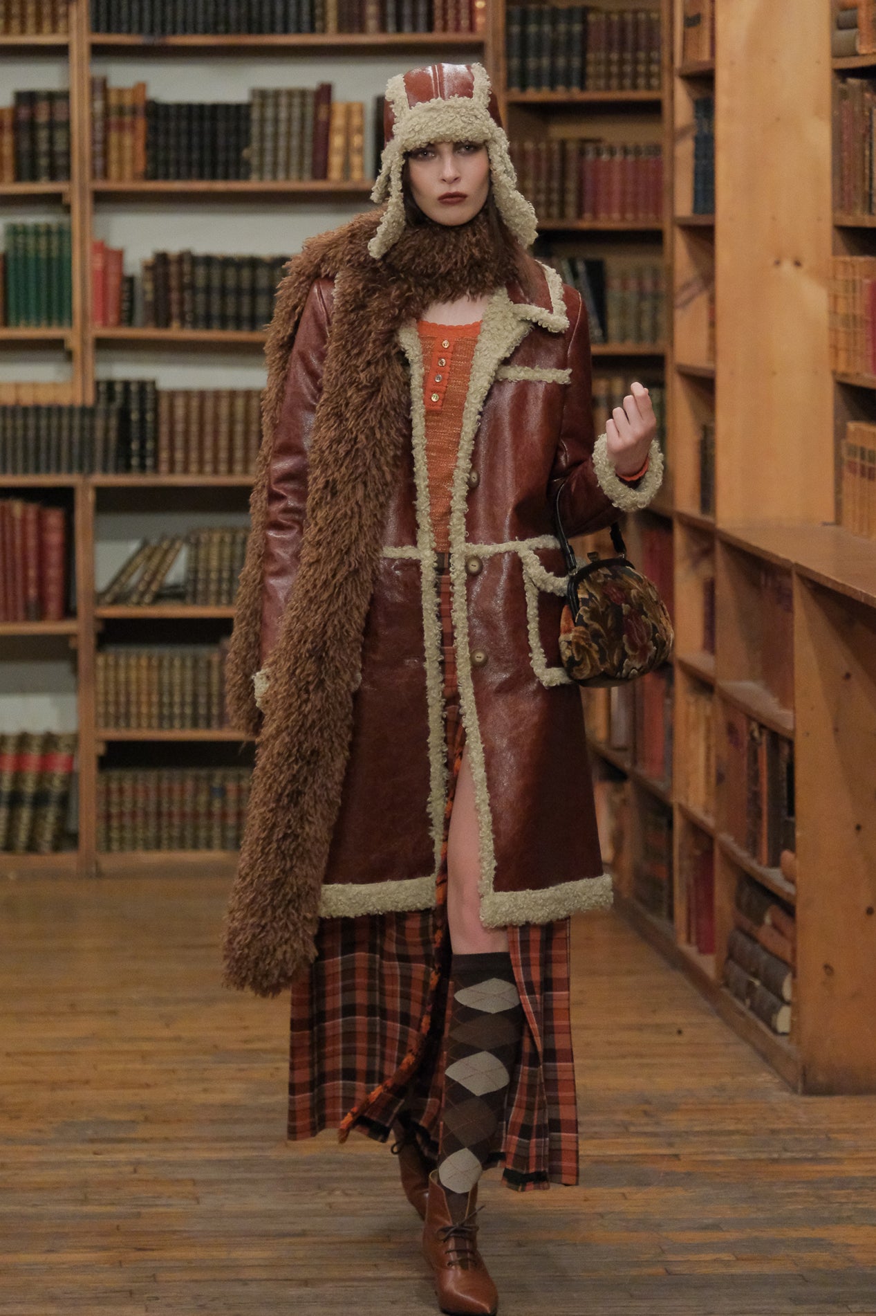 In a library, Tobacco Faux Leather with Curly Lamb Trim Aviator Hat paired with tobacco coat