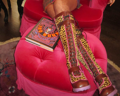 Woman on an ottoman with Leopard print boots with brown/purple accent, buckle on front and side.