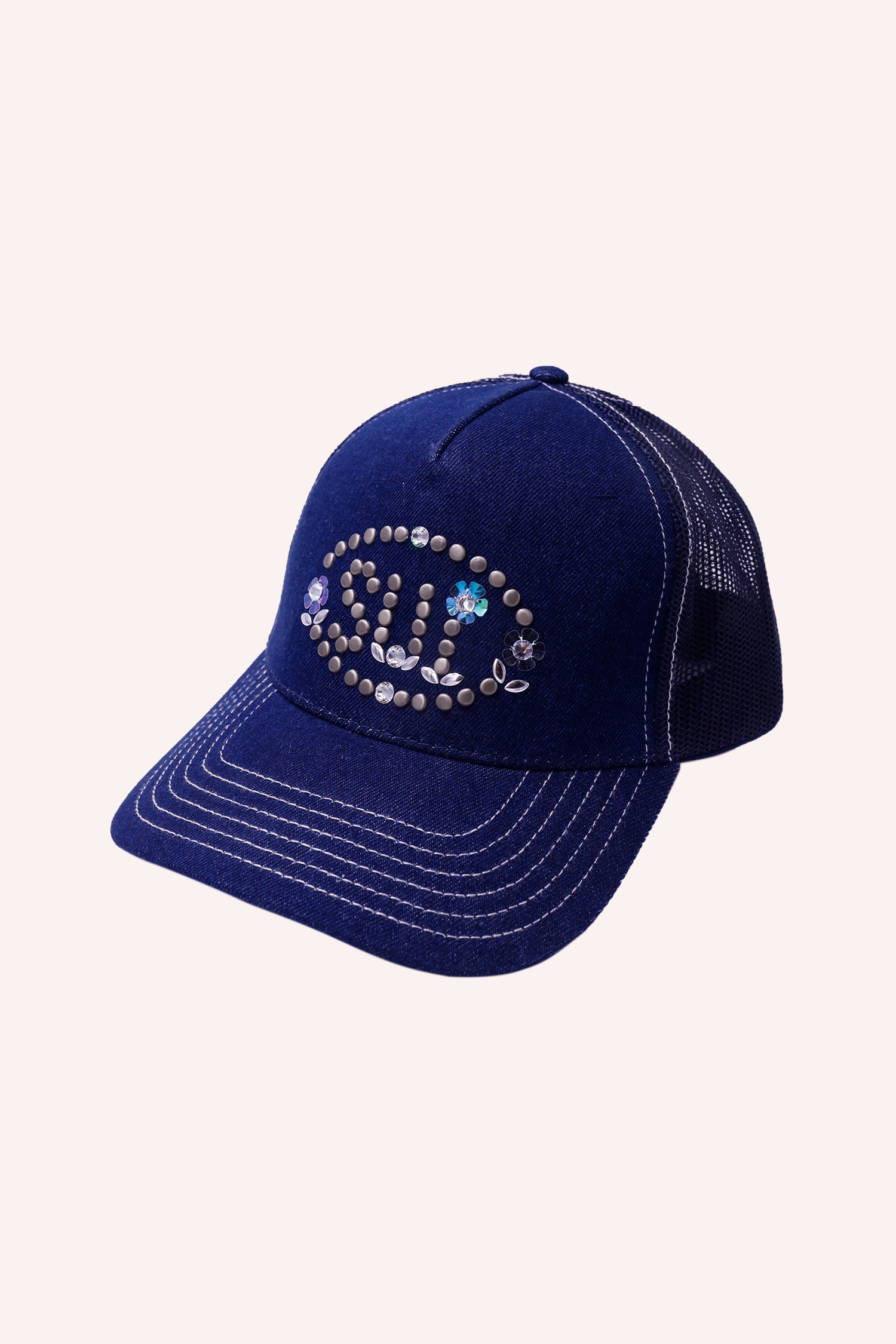 Dark denim baseball hat with white stitches and studded Anna Sui logo inside an oval with a floral design