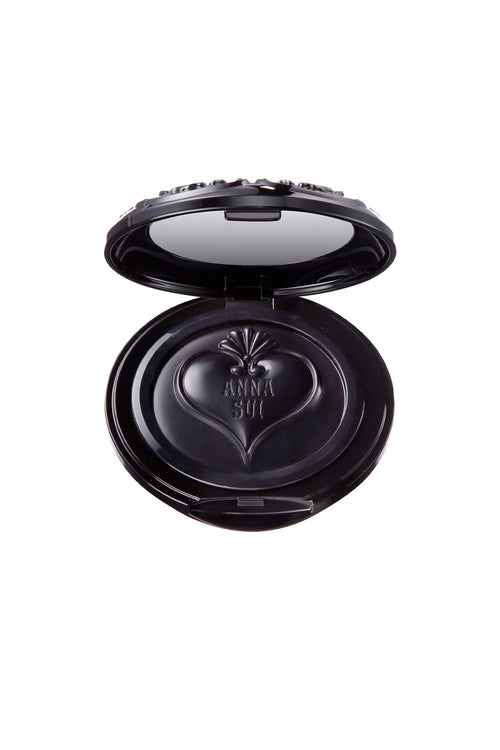 Cream blush in an open round black container, a mirror into the top lid, a heart-shaped lid with Anna Sui branding on blush.