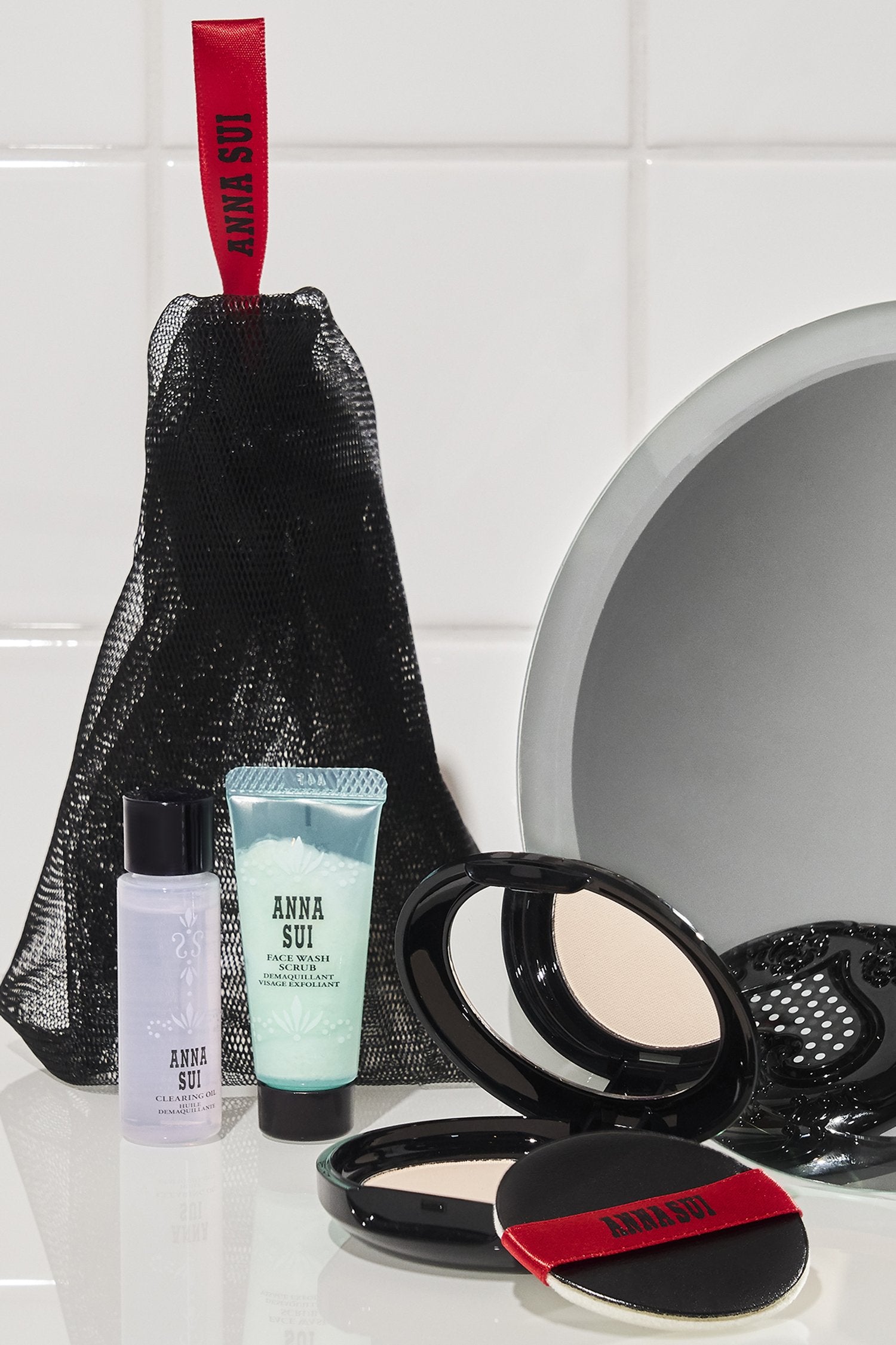 Face Wash Scrub, Clearing Lotion, Powder Container, and a Net-Like Bag on a Bathroom Countertop