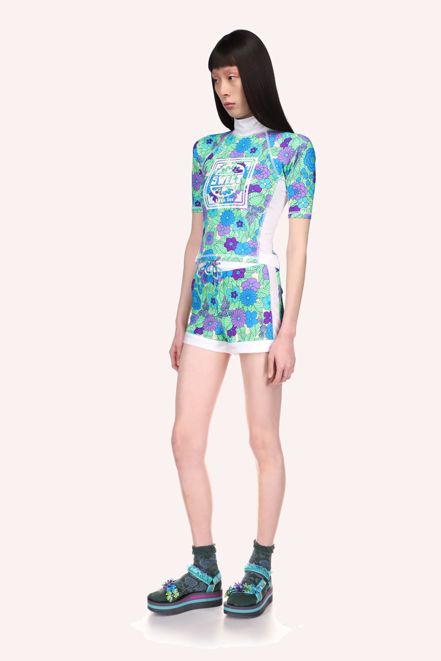 Beckoning Blossoms Surf Shorts, floral design in blue, purple light and dark on a green leaves background